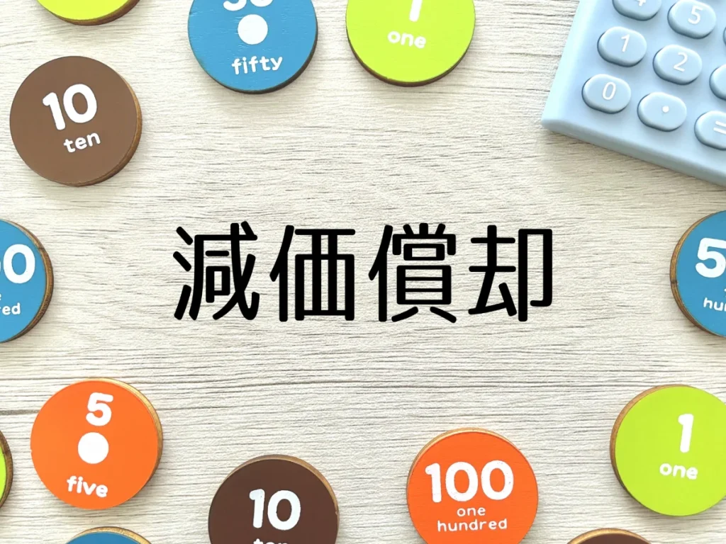 「減価償却」の文字と数字の書かれたコイン、電卓(不動産の減価償却)